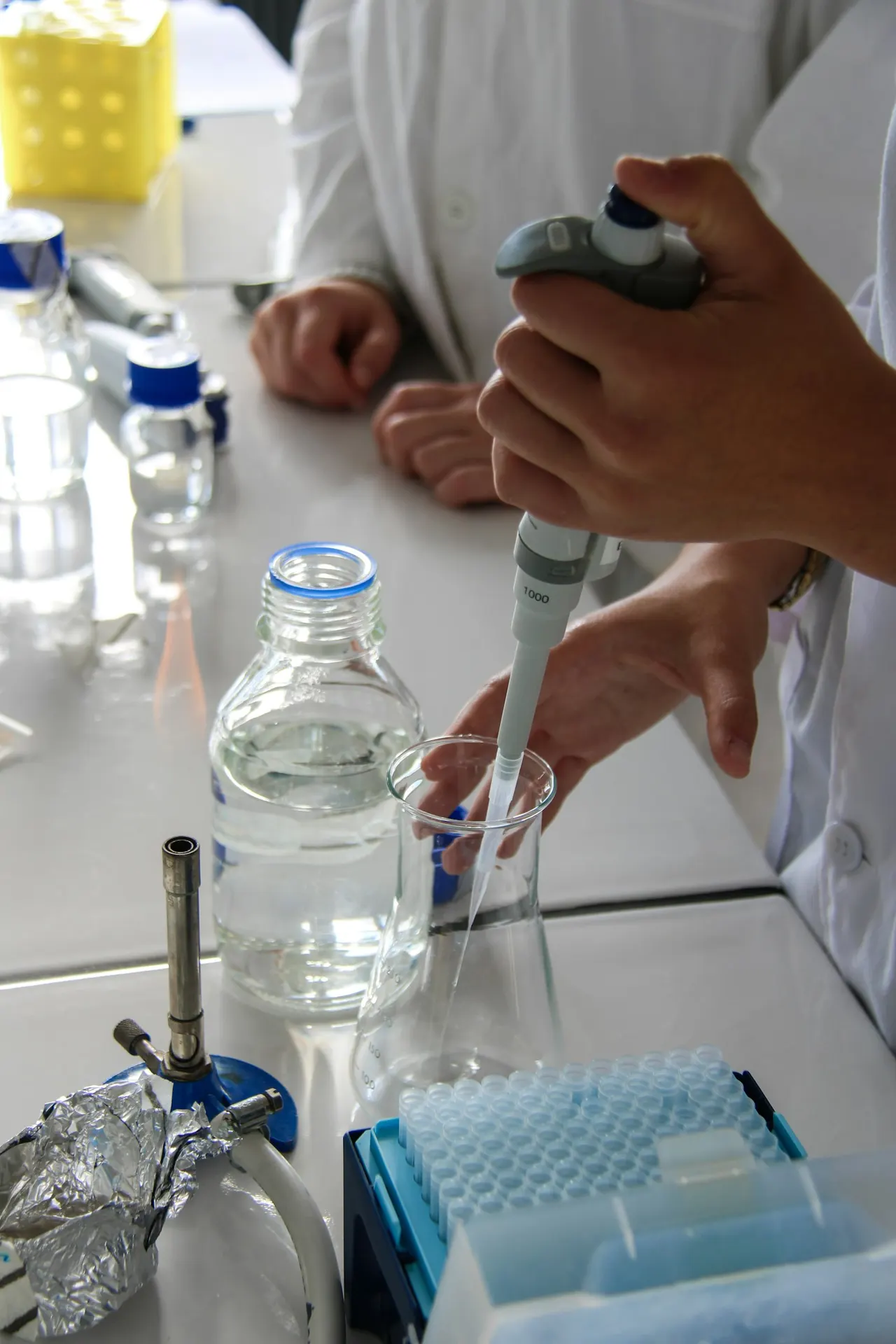 Gloved hands pipetting liquid into a glass bottle