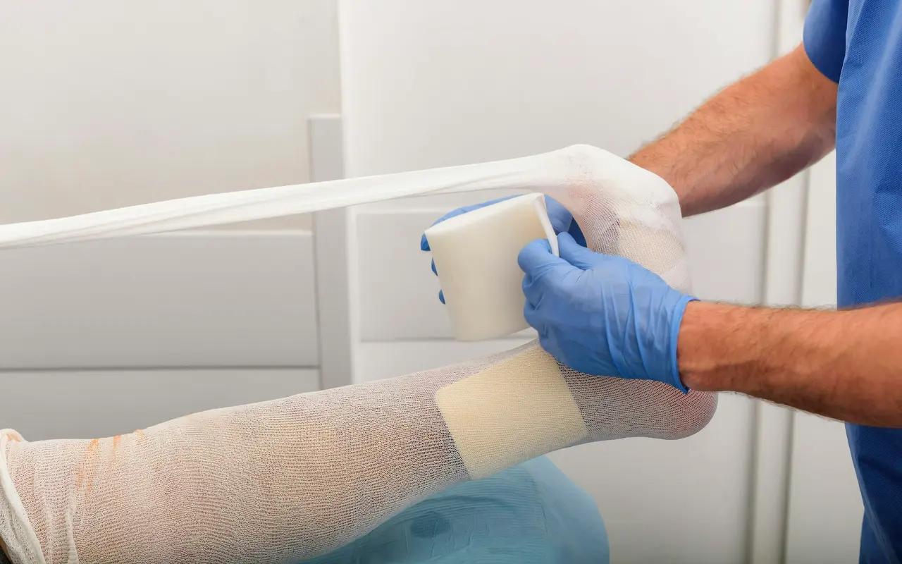 Gloved hands applying a foam dressing and tubular bandage to a leg
